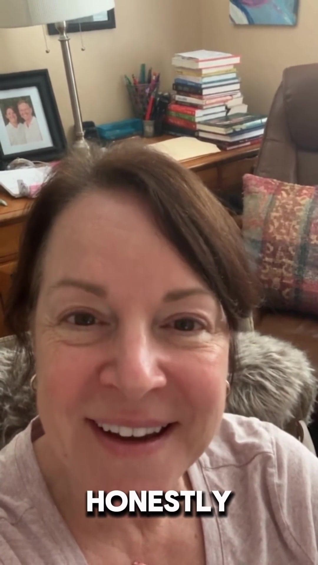 Smiling woman recording a video with books and framed photos behind her